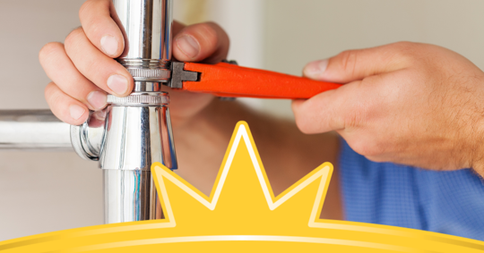 a plumber tightening a pipe with an orange wrench.